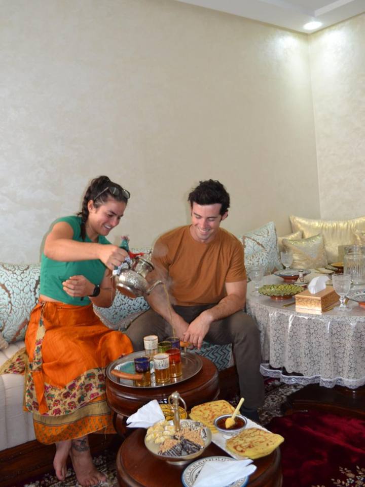 Guest in an orange caftan pouring mint tea in the salon