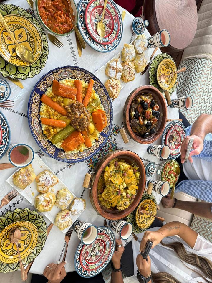 Overhead view of a dinner table with couscous, tagines, pastilla, salads and tea glasses