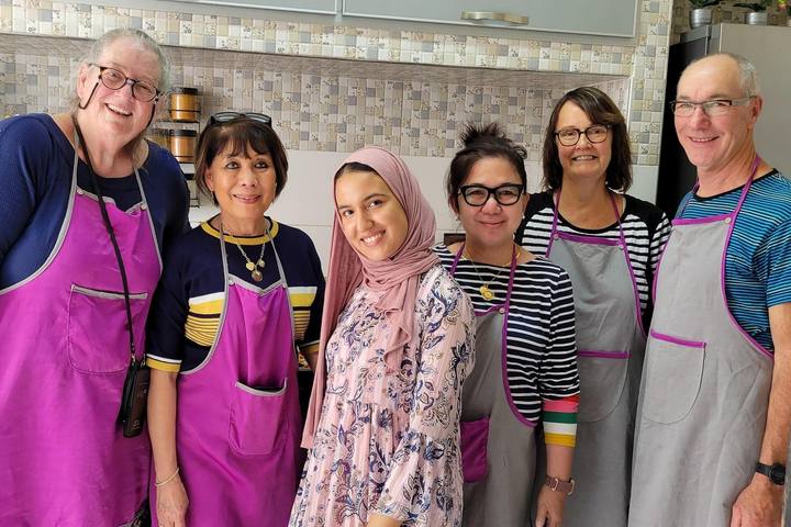 Group of guests in pink aprons with the hosts in the kitchen